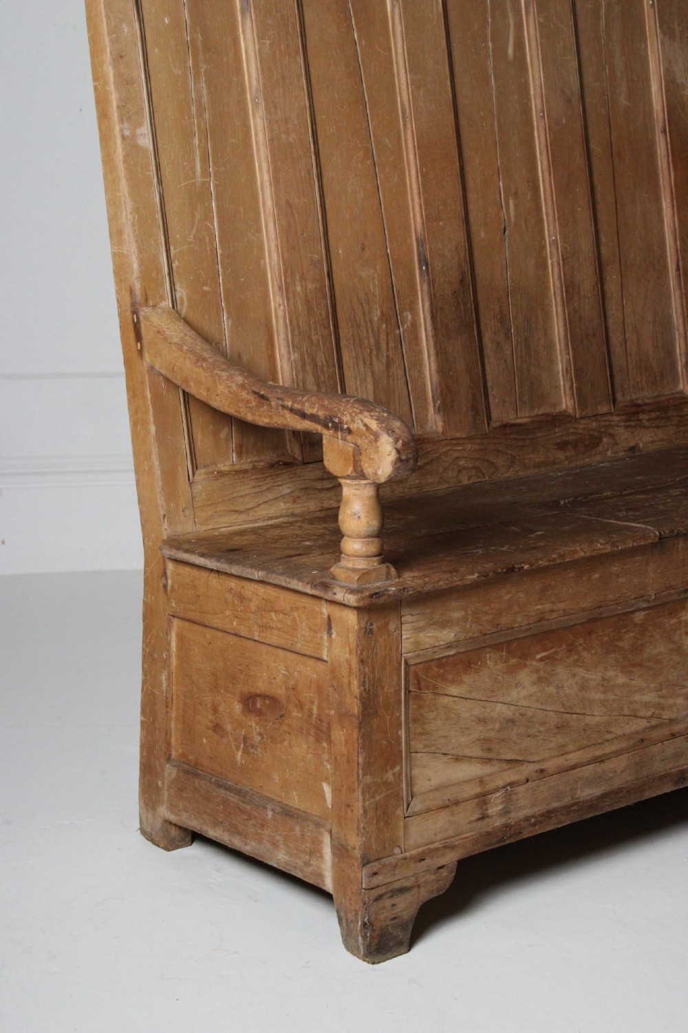 A 19th-century pine box settle featuring a high panelled back rest, curved armrests on turned supports, and an enclosed base incorporating a seat storage compartment. View VI
