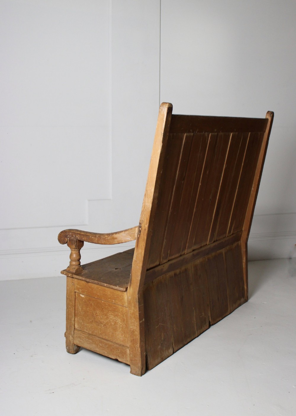 A 19th-century pine box settle featuring a high panelled back rest, curved armrests on turned supports, and an enclosed base incorporating a seat storage compartment. View VII