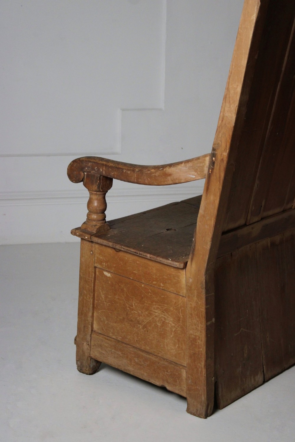 A 19th-century pine box settle featuring a high panelled back rest, curved armrests on turned supports, and an enclosed base incorporating a seat storage compartment. View VIII