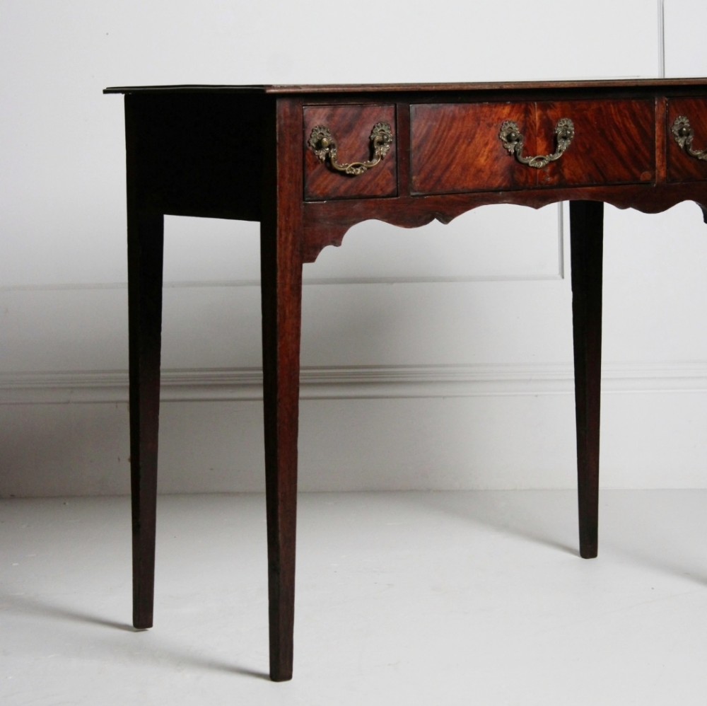 An 18th-century Georgian mahogany side table with three frieze drawers, brass swan-neck handles, a shaped apron, and tapered square legs. View II