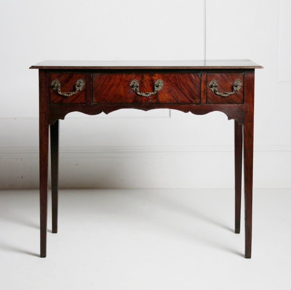 An 18th-century Georgian mahogany side table with three frieze drawers, brass swan-neck handles, a shaped apron, and tapered square legs. View IV