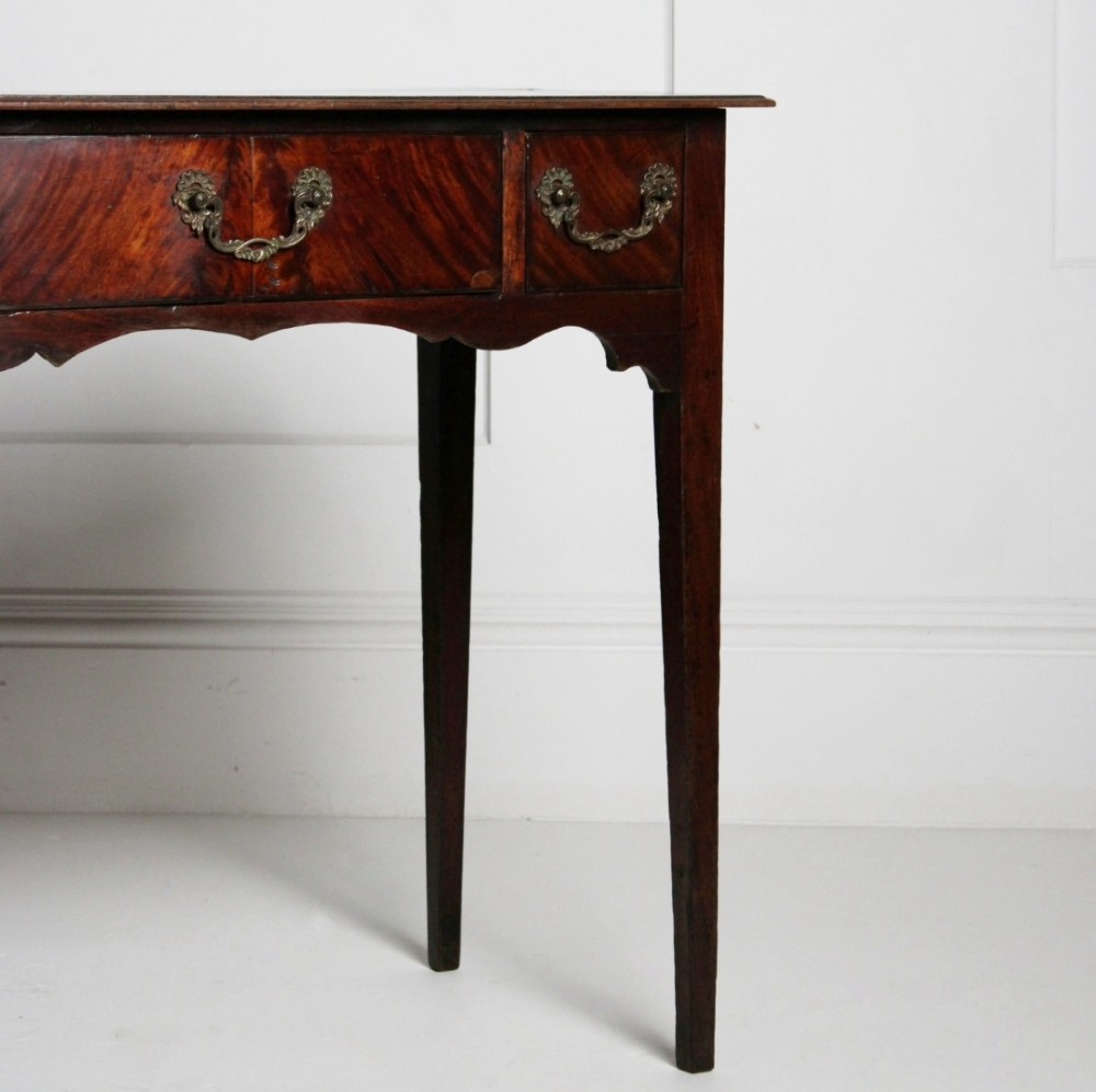 An 18th-century Georgian mahogany side table with three frieze drawers, brass swan-neck handles, a shaped apron, and tapered square legs. View V