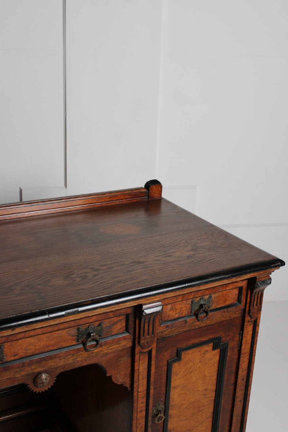 An Aesthetic Movement kneehole writing desk in walnut with ebonised borders, three upper drawers, two pedestal cupboards, and brass ring handles. View II