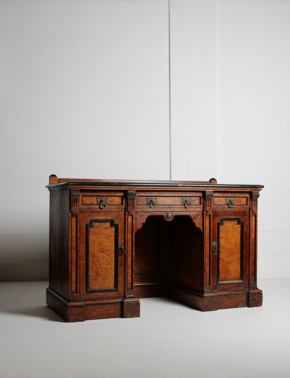 An Aesthetic Movement kneehole writing desk in walnut with ebonised borders, three upper drawers, two pedestal cupboards, and brass ring handles.