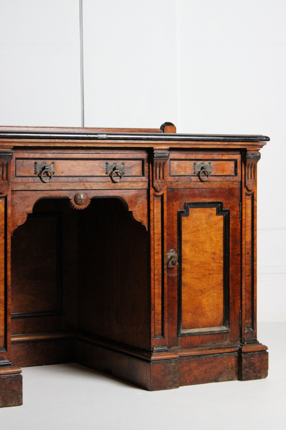 An Aesthetic Movement kneehole writing desk in walnut with ebonised borders, three upper drawers, two pedestal cupboards, and brass ring handles. View V
