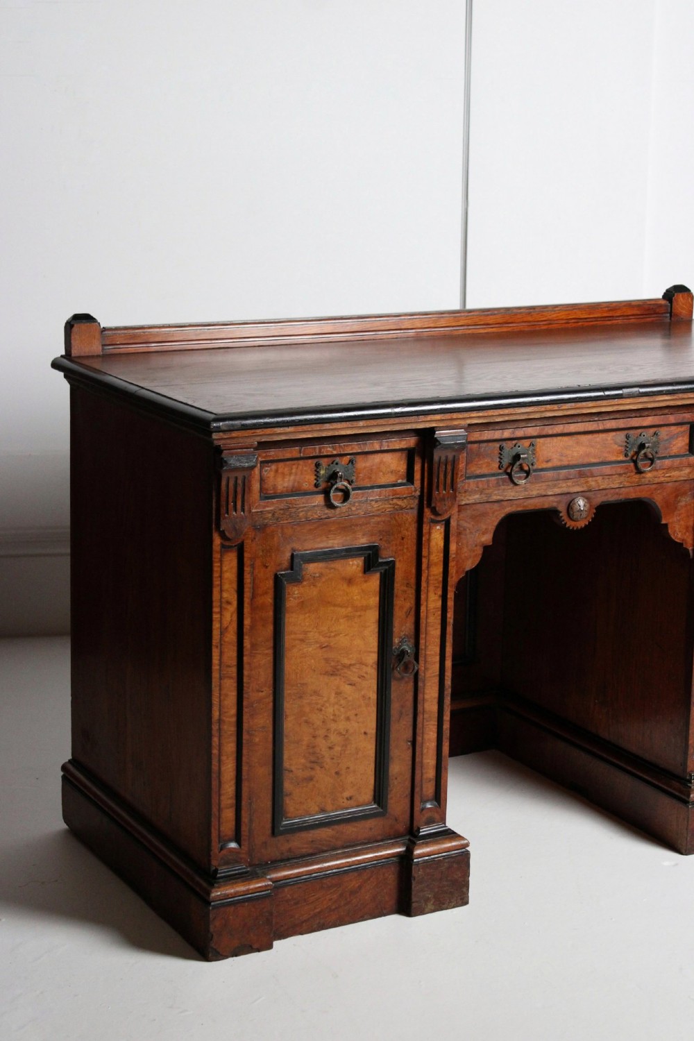 An Aesthetic Movement kneehole writing desk in walnut with ebonised borders, three upper drawers, two pedestal cupboards, and brass ring handles. View VI