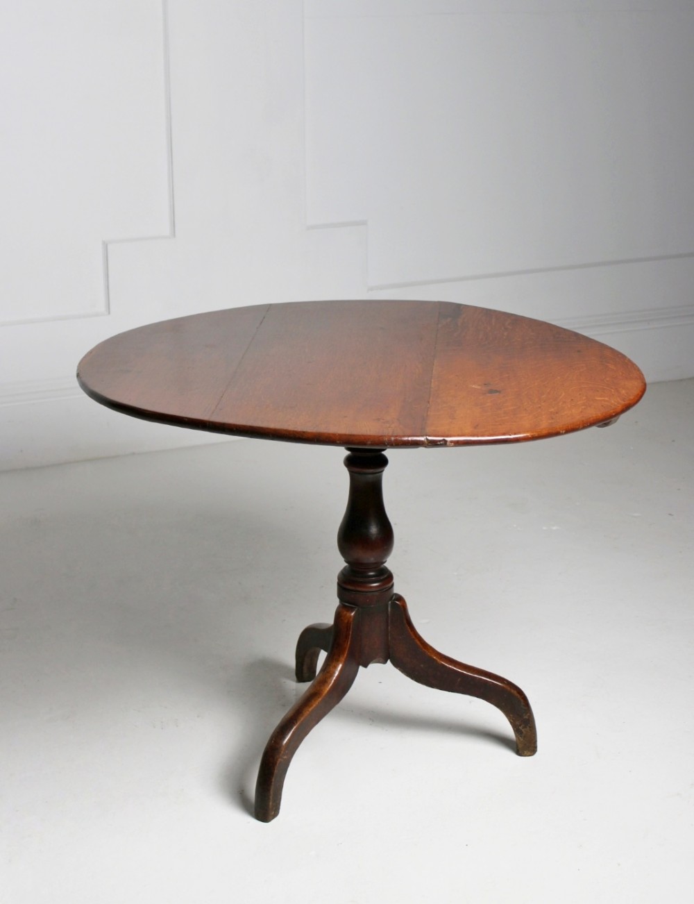An 18th-century circular oak tilt-top table shown in a vertically tilted position on a turned tripod base. View V