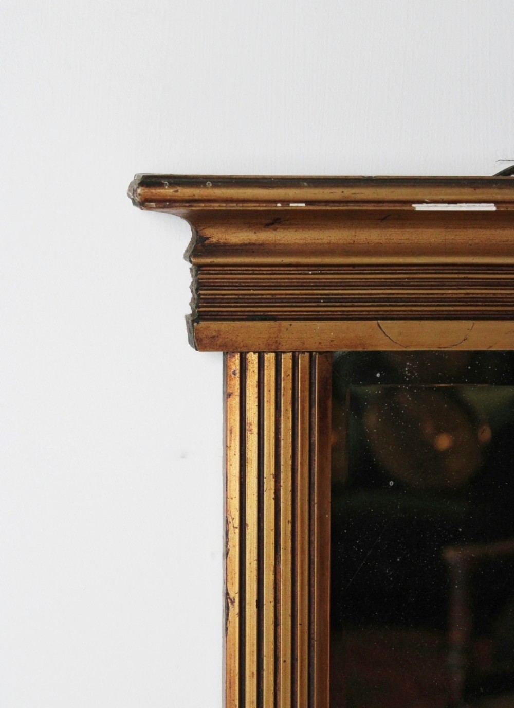 An early 19th century Regency giltwood pier mirror with reeded pilaster sides, a stepped architectural cornice, and foxed glass mirror plate. View II