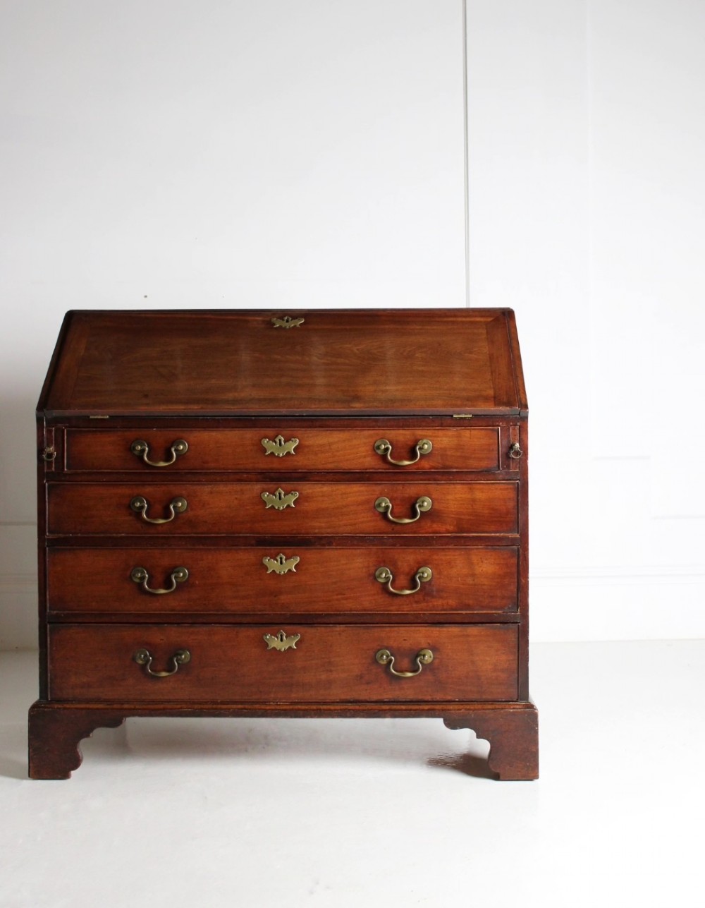A George III mahogany fall front bureau featuring four graduated drawers with brass handles, resting on bracket feet.