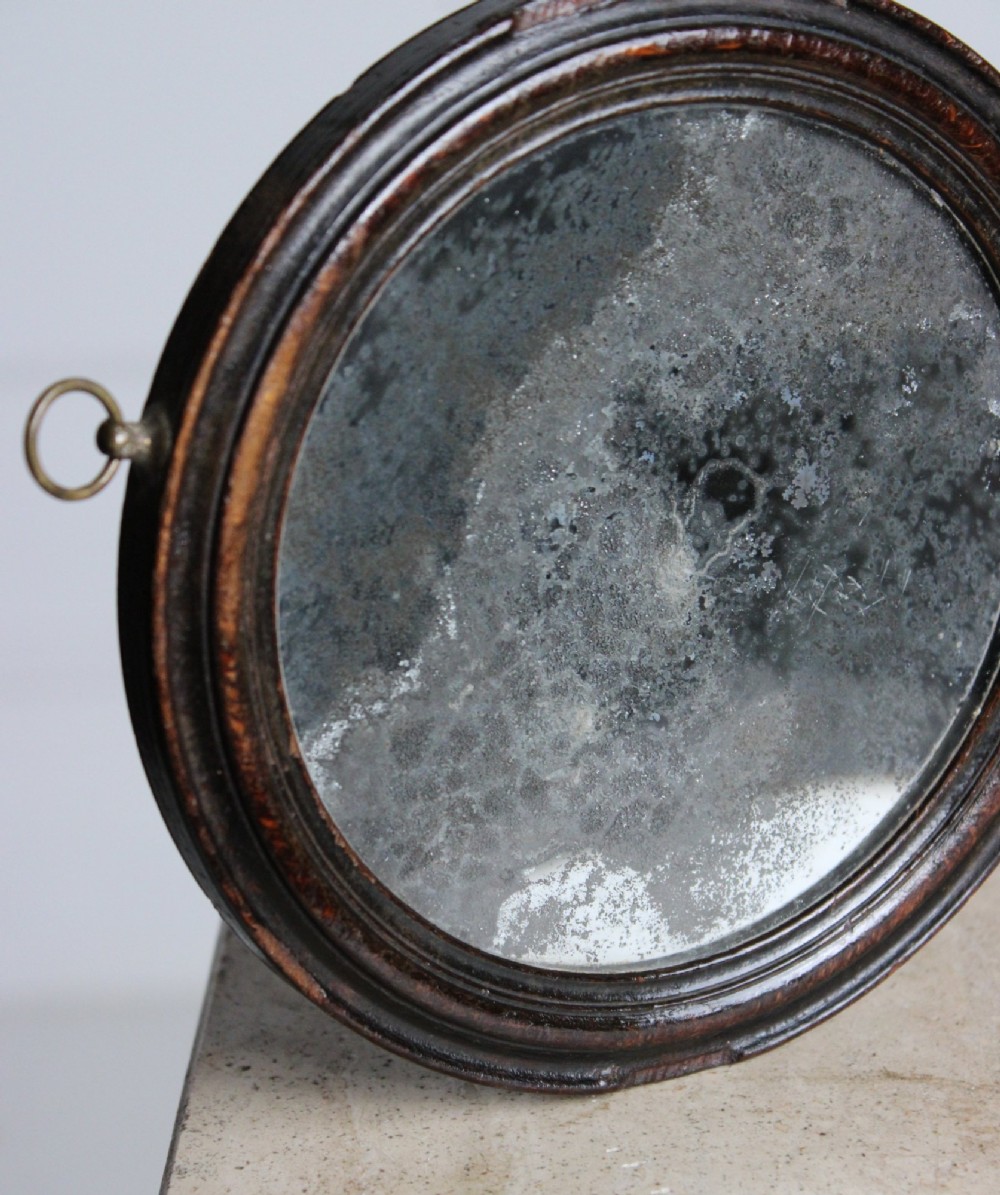 A circular Georgian wooden hand mirror with a turned handle, dark brown finish, top brass hanging loop, and foxed mirror glass. View II