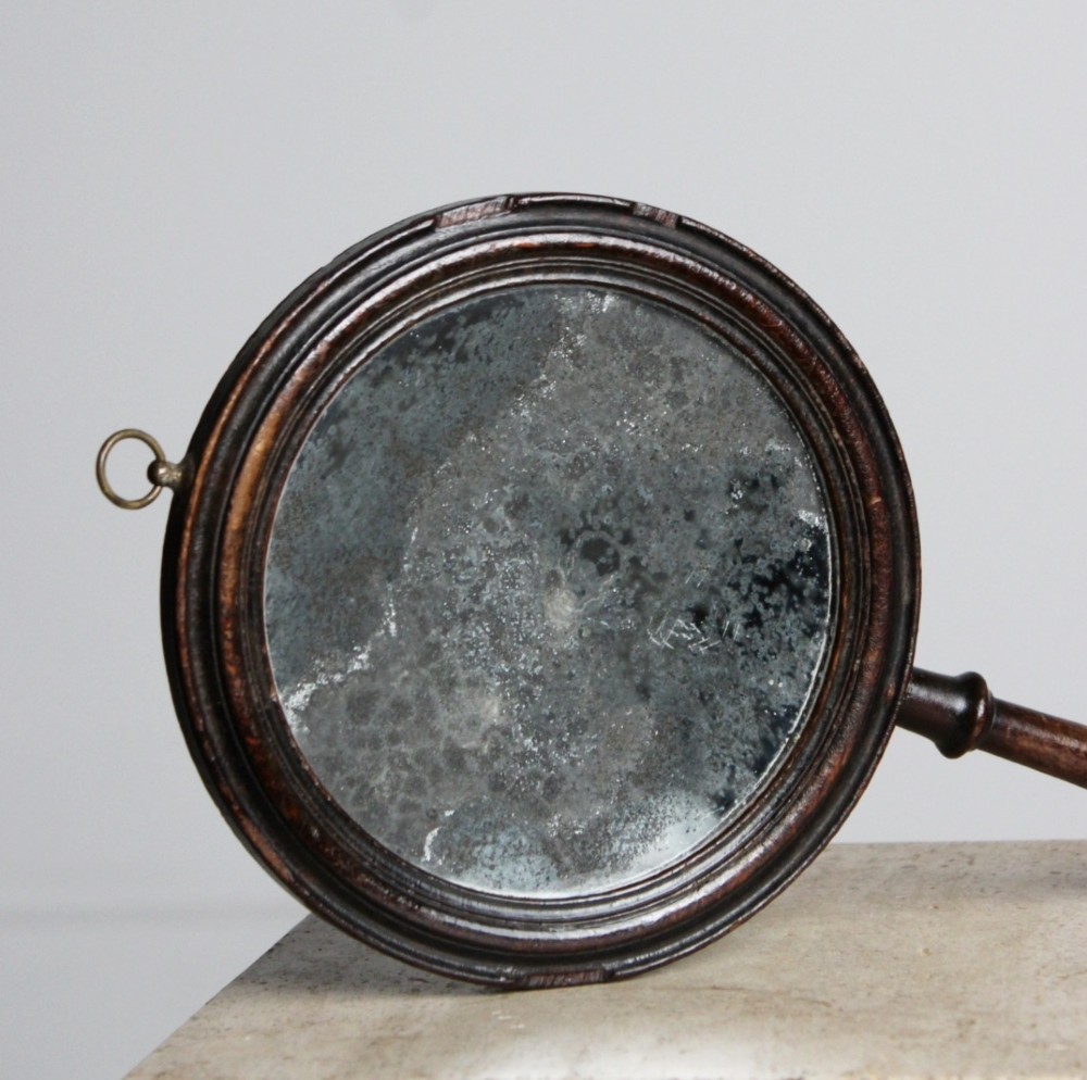 A circular Georgian wooden hand mirror with a turned handle, dark brown finish, top brass hanging loop, and foxed mirror glass. View IV