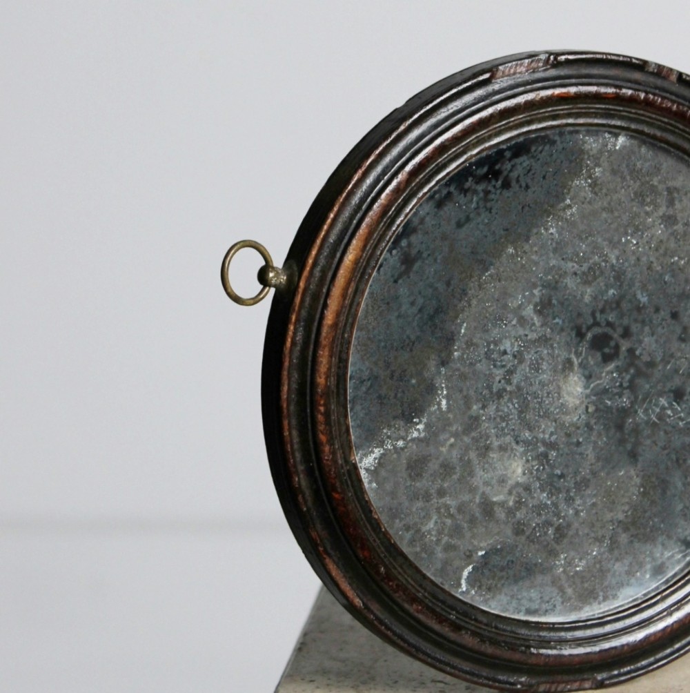 A circular Georgian wooden hand mirror with a turned handle, dark brown finish, top brass hanging loop, and foxed mirror glass. View V