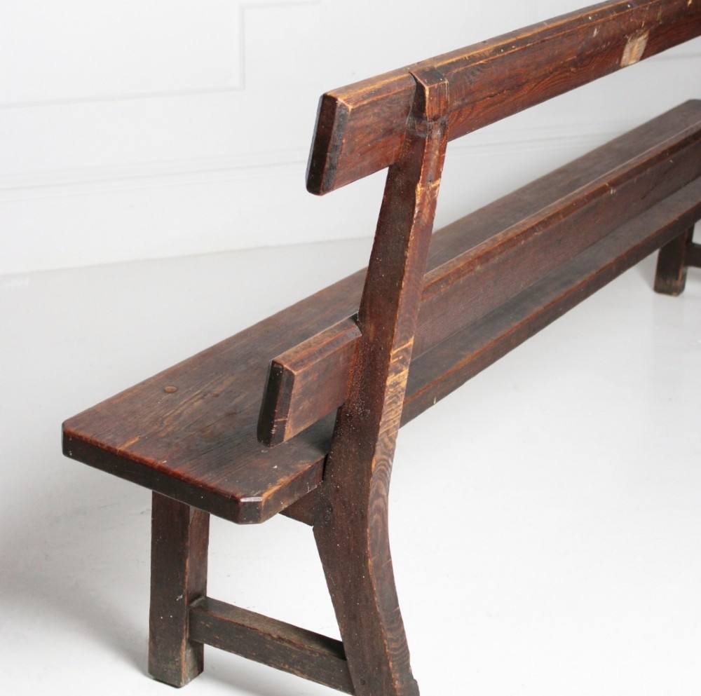 A long 19th century stained pine bench featuring a two-rail backrest and splayed legs connected by side stretchers. View II