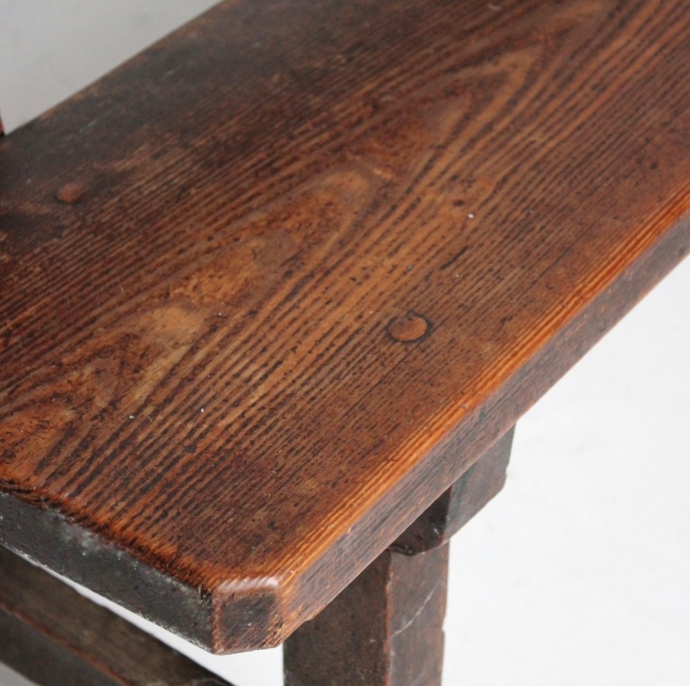 A long 19th century stained pine bench featuring a two-rail backrest and splayed legs connected by side stretchers. View III