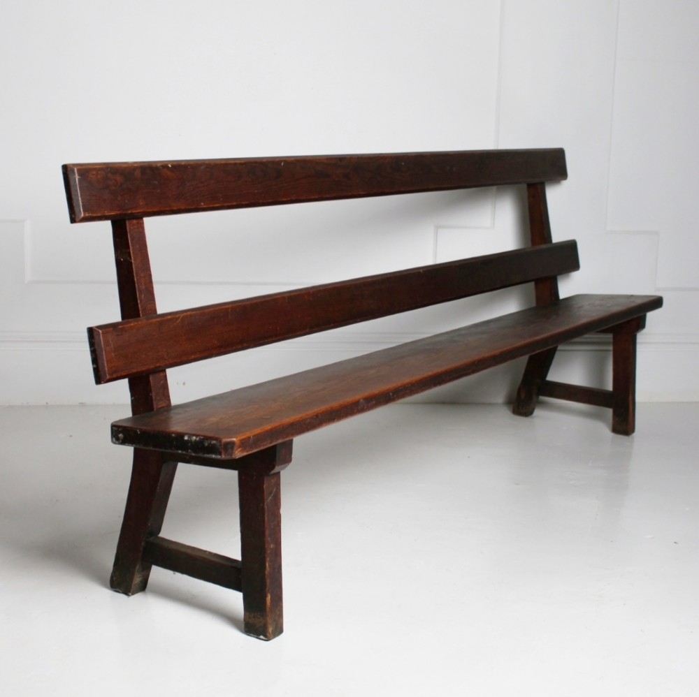 A long 19th century stained pine bench featuring a two-rail backrest and splayed legs connected by side stretchers.