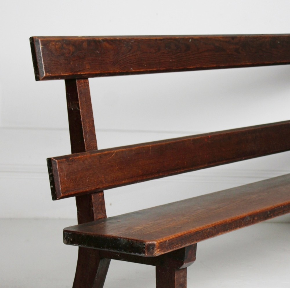 A long 19th century stained pine bench featuring a two-rail backrest and splayed legs connected by side stretchers. View IV