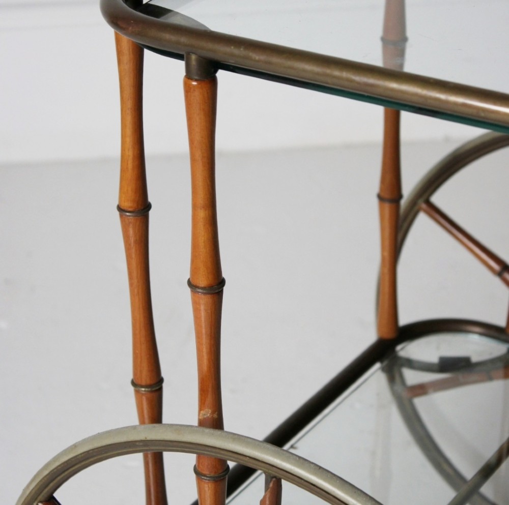 A two-tier mid-century drinks trolley featuring a faux bamboo brass and wood frame, clear glass shelves, two large spoked wheels, and small rear castors. View IV