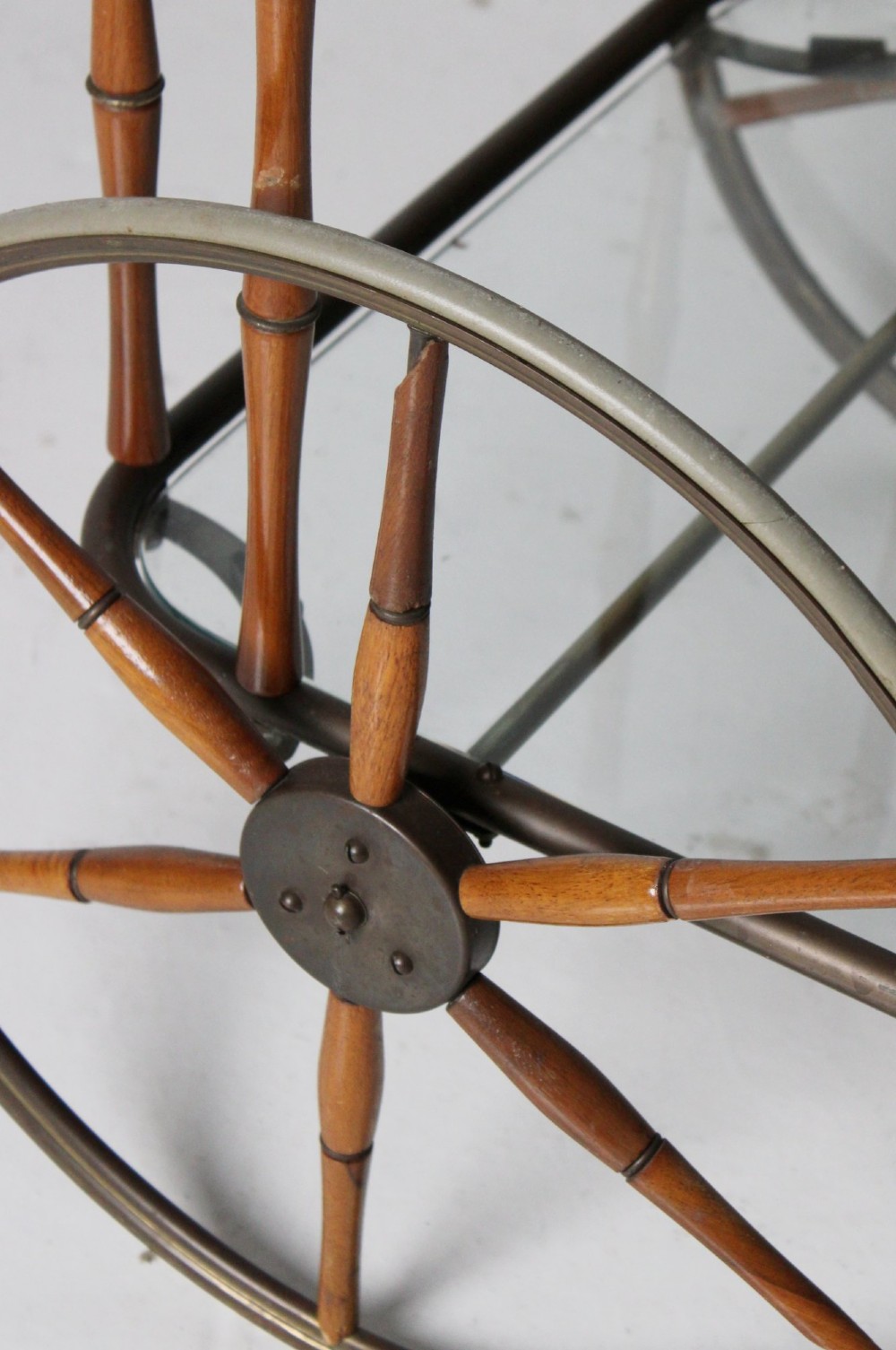 A two-tier mid-century drinks trolley featuring a faux bamboo brass and wood frame, clear glass shelves, two large spoked wheels, and small rear castors. View V