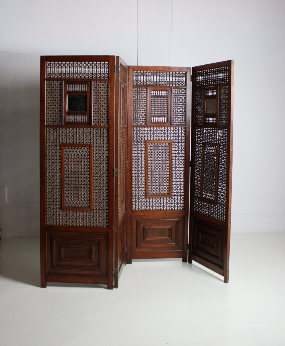A four-panel dark hardwood folding screen featuring intricate geometric mashrabiya latticework panels above carved recessed bottom sections. View VI