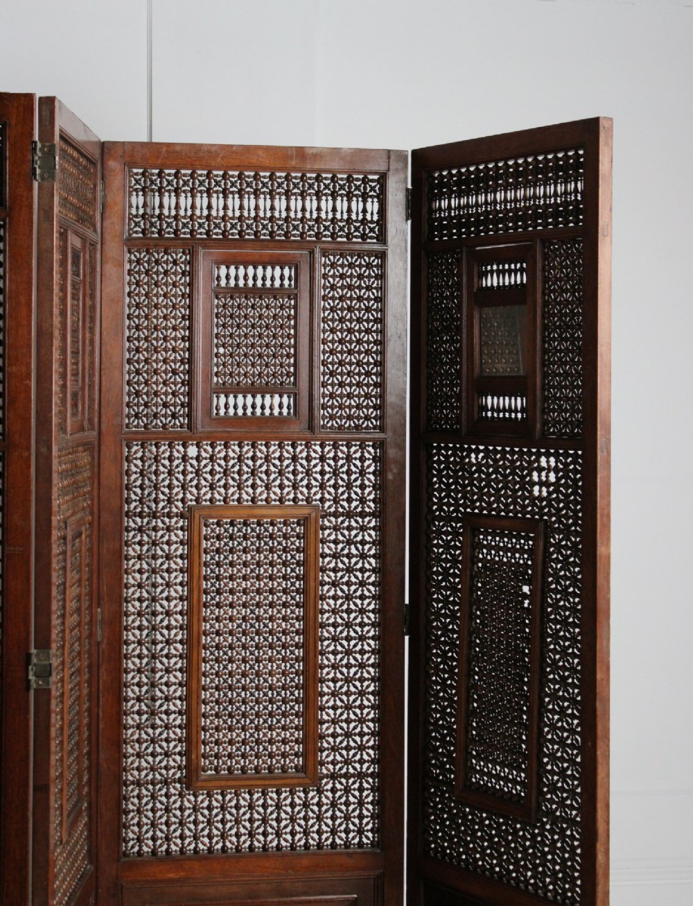 A four-panel dark hardwood folding screen featuring intricate geometric mashrabiya latticework panels above carved recessed bottom sections. View VII
