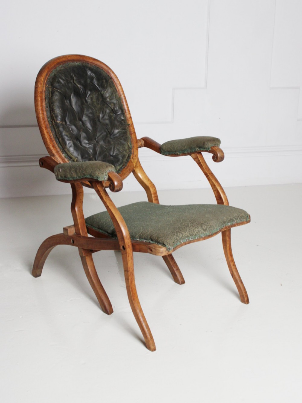 An antique birds eye maple folding armchair featuring curved legs, padded armrests, an oval backrest, and green textured upholstery. View II