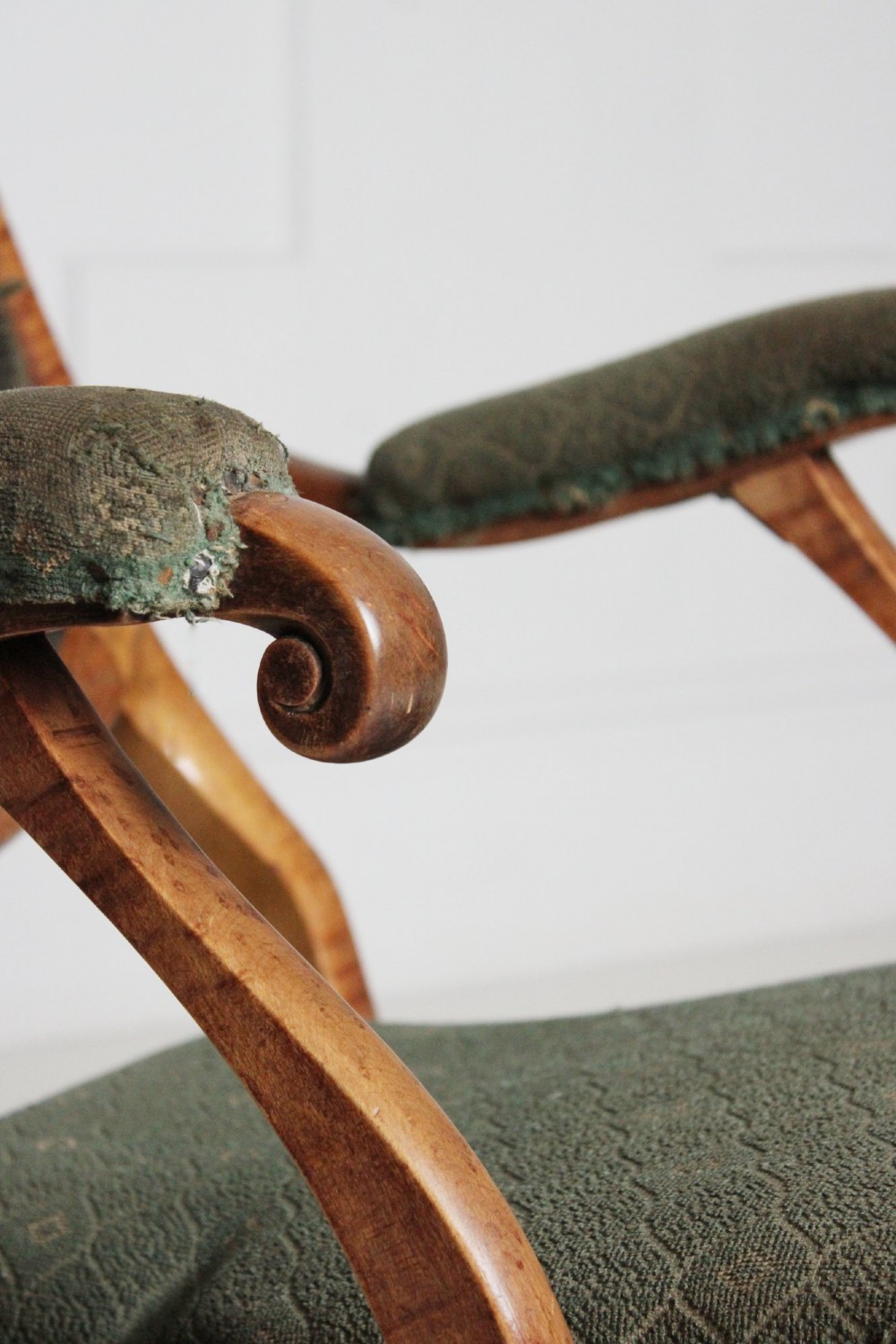 An antique birds eye maple folding armchair featuring curved legs, padded armrests, an oval backrest, and green textured upholstery. View III