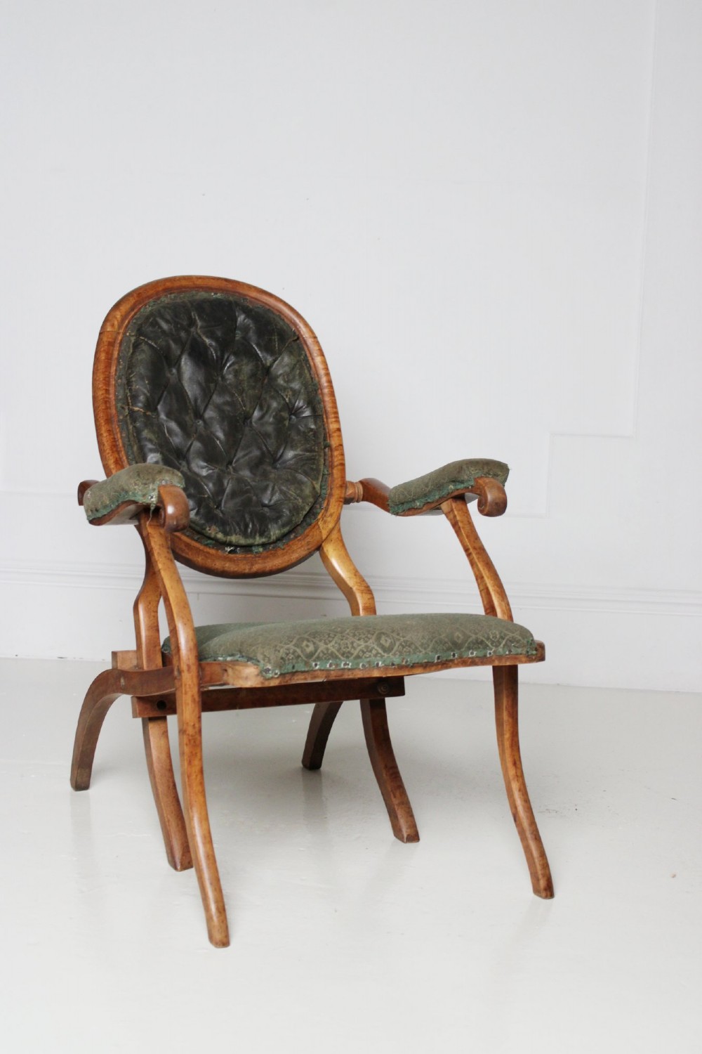 An antique birds eye maple folding armchair featuring curved legs, padded armrests, an oval backrest, and green textured upholstery. View IV