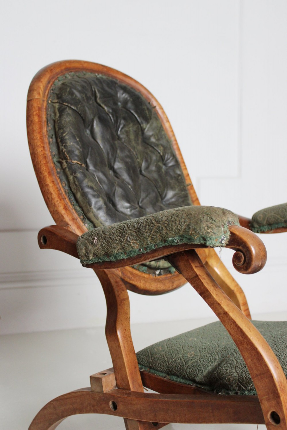 An antique birds eye maple folding armchair featuring curved legs, padded armrests, an oval backrest, and green textured upholstery. View V