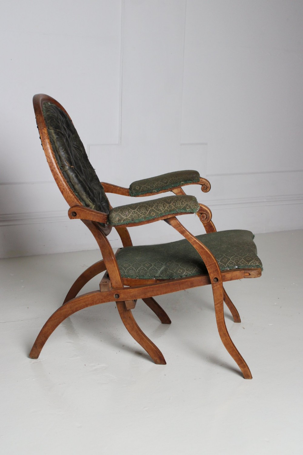 An antique birds eye maple folding armchair featuring curved legs, padded armrests, an oval backrest, and green textured upholstery. View VI