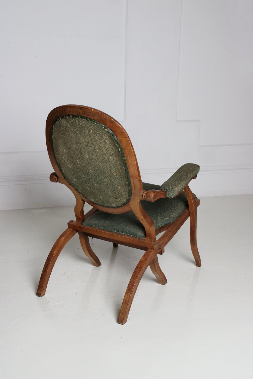An antique birds eye maple folding armchair featuring curved legs, padded armrests, an oval backrest, and green textured upholstery. View VII