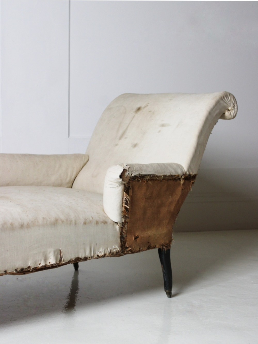 A Victorian country house daybed upholstered in cream calico, featuring turned ebonised legs on brass castors and a scrolled backrest. View II