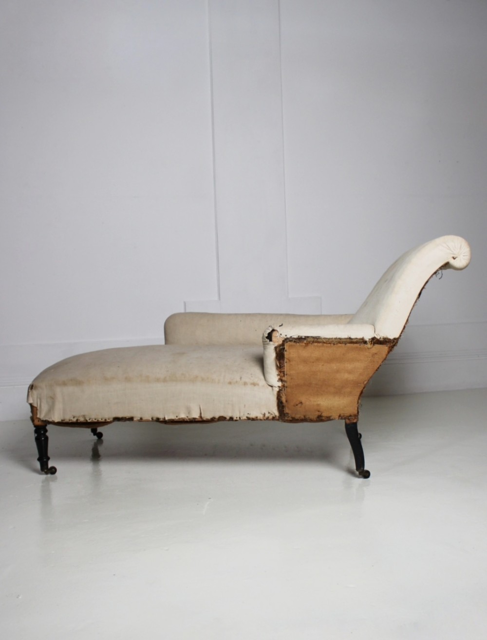 A Victorian country house daybed upholstered in cream calico, featuring turned ebonised legs on brass castors and a scrolled backrest. View III