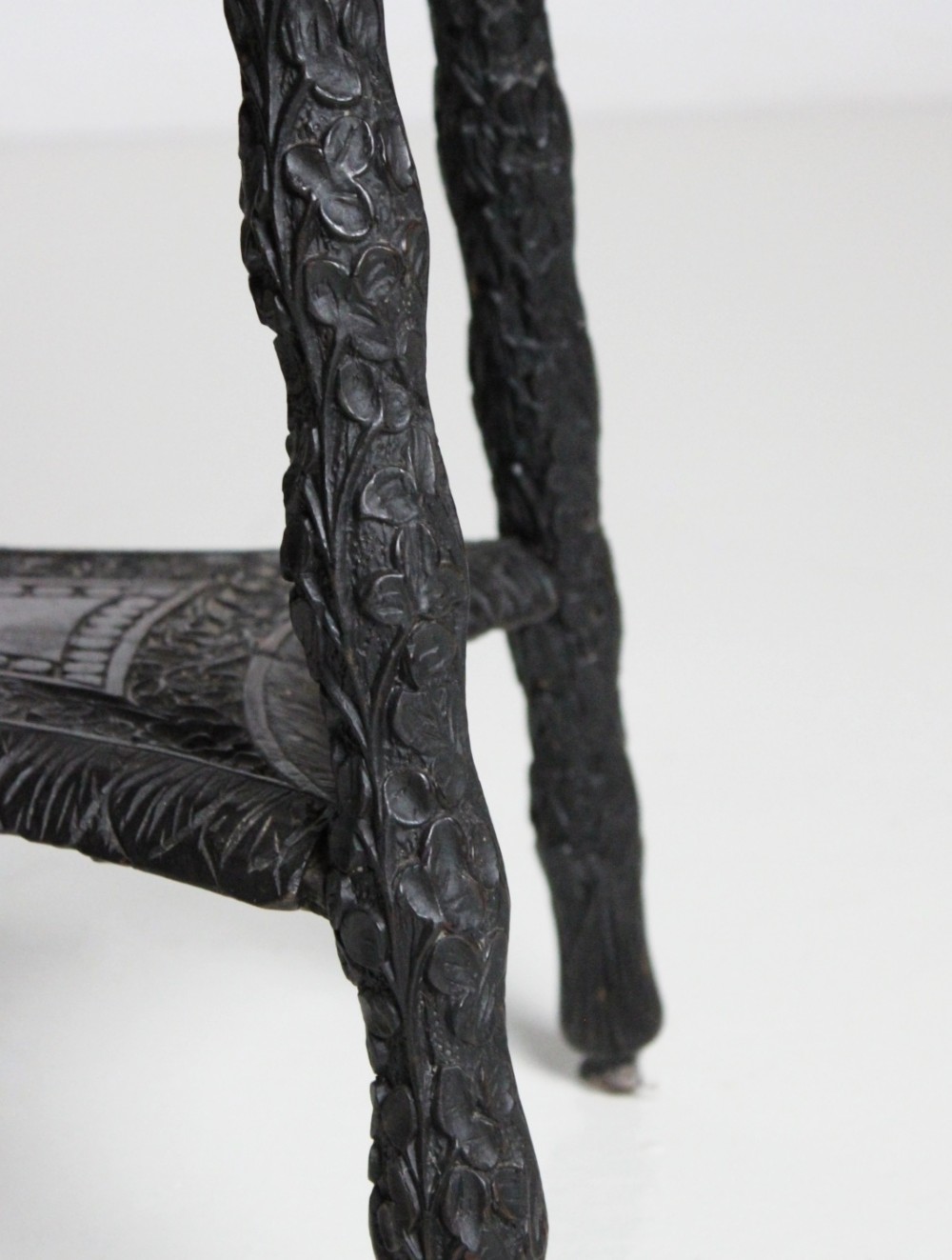An oval dark timber Anglo-Indian side table featuring hand-carved floral borders, four textured legs, and a carved lower undertier shelf. View II