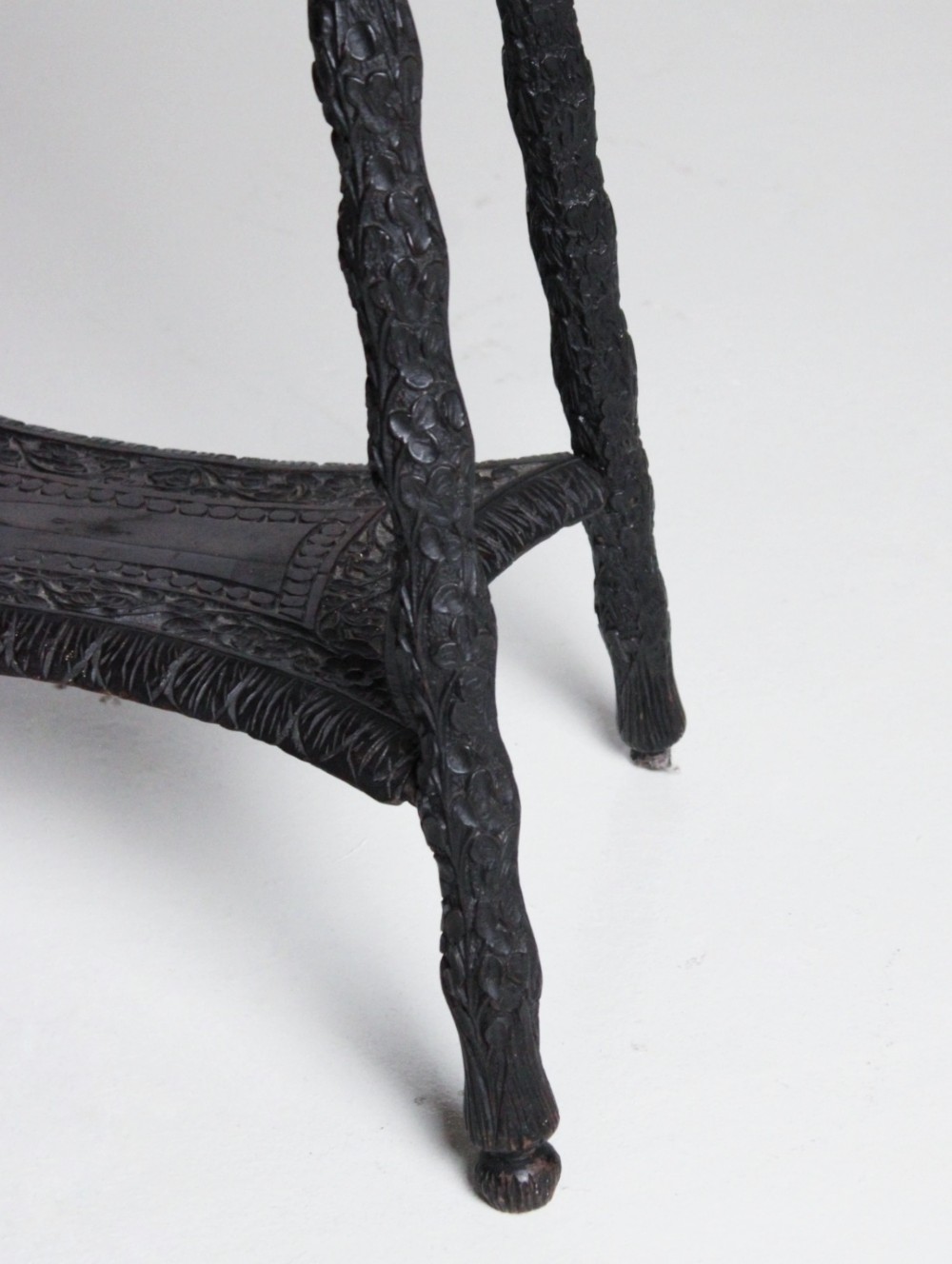 An oval dark timber Anglo-Indian side table featuring hand-carved floral borders, four textured legs, and a carved lower undertier shelf. View IV