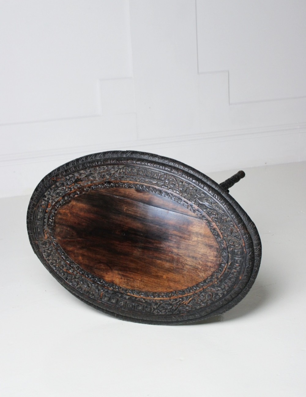 An oval dark timber Anglo-Indian side table featuring hand-carved floral borders, four textured legs, and a carved lower undertier shelf. View V