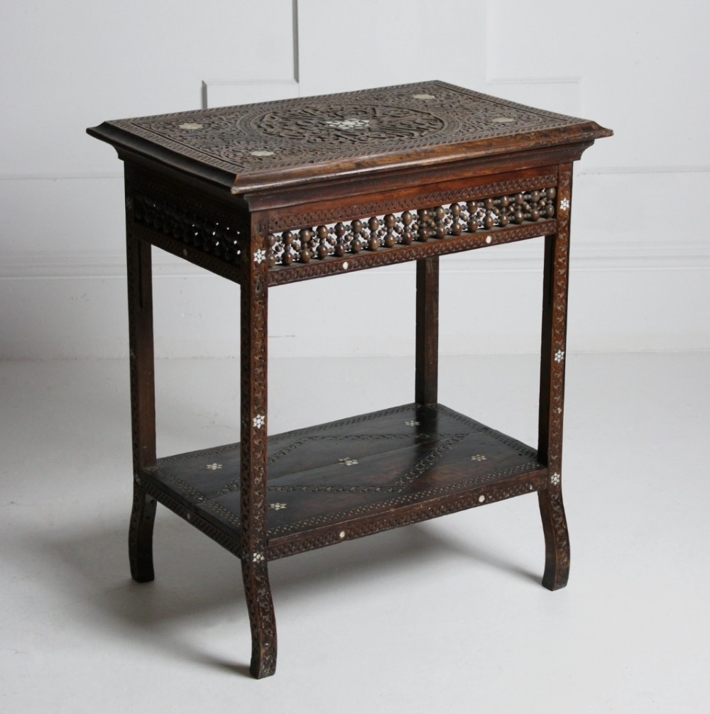 A 19th-century dark brown wooden Syrian two-tier side table featuring intricate carving, mother-of-pearl inlay, and turned lattice friezes.