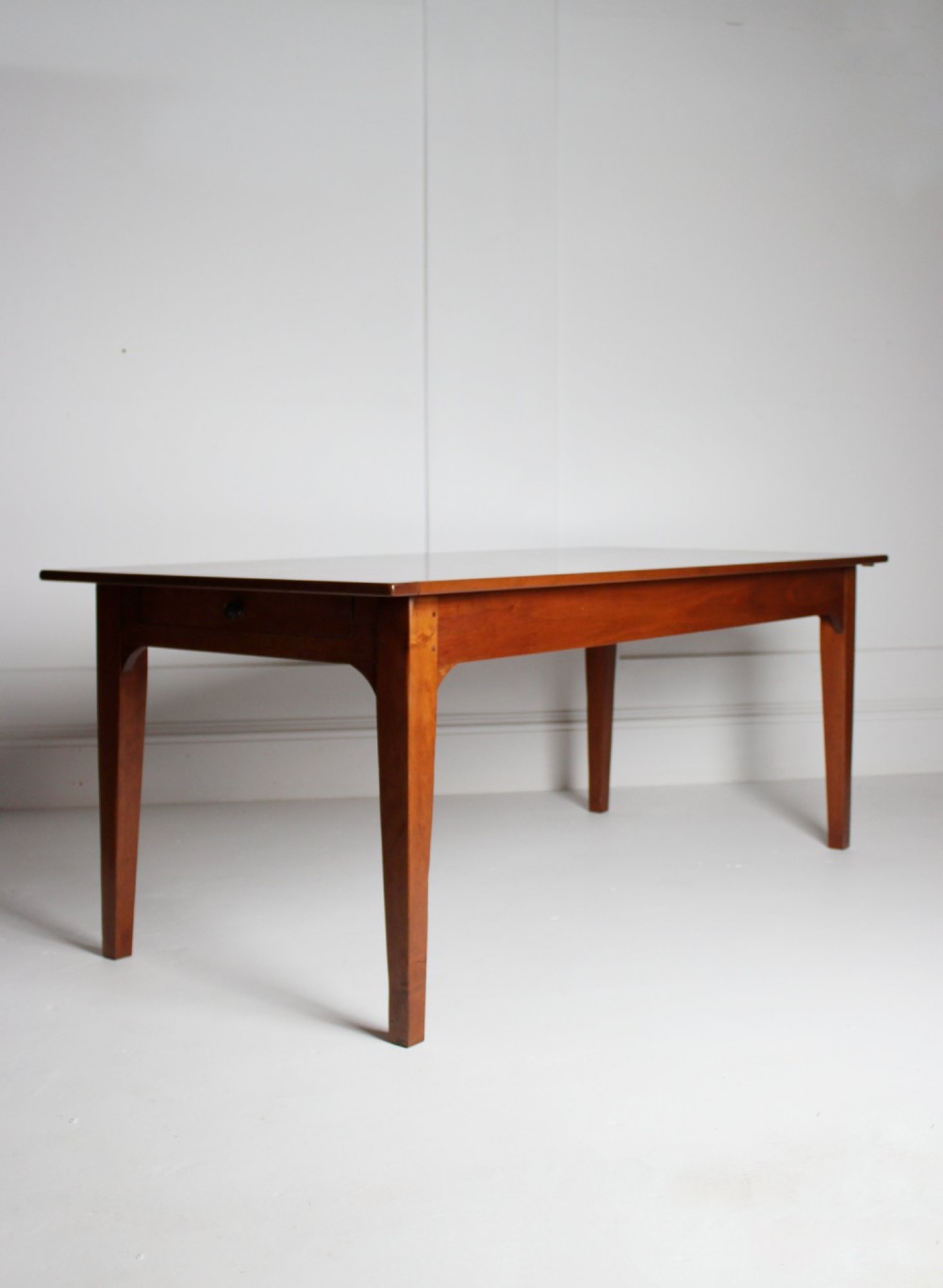 A rectangular French cherrywood dining table featuring tapered legs, a plain apron, and an end drawer with a dark circular pull knob.