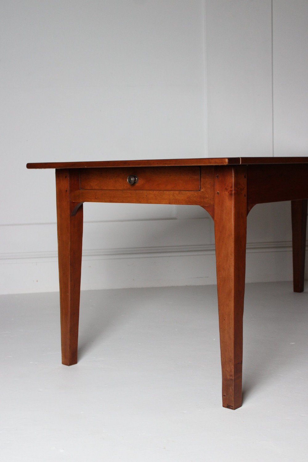 A rectangular French cherrywood dining table featuring tapered legs, a plain apron, and an end drawer with a dark circular pull knob. View IV