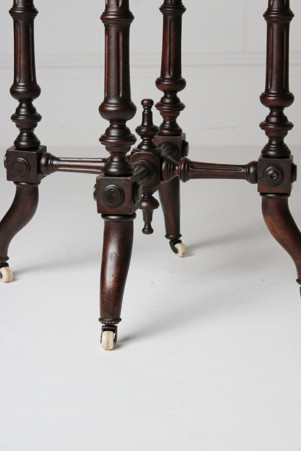 A dark timber Aesthetic Movement side table featuring turned legs, splayed feet on castors, an intricate lower stretcher, and a yellow fabric-covered top finished with fringe trim. View III