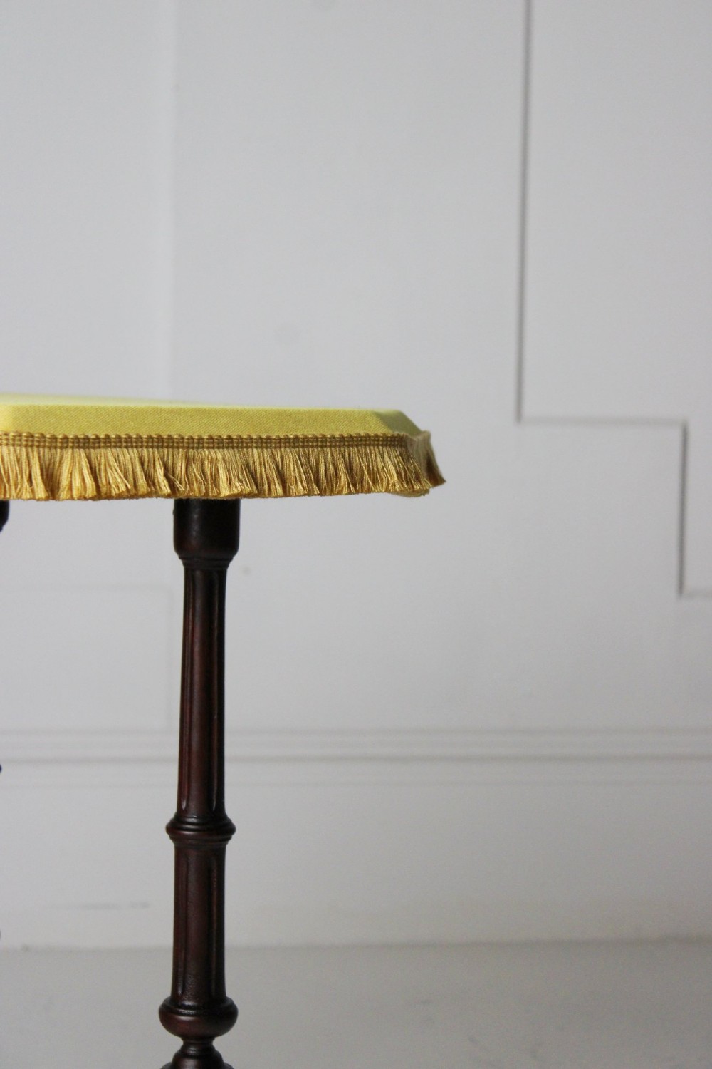 A dark timber Aesthetic Movement side table featuring turned legs, splayed feet on castors, an intricate lower stretcher, and a yellow fabric-covered top finished with fringe trim. View IV