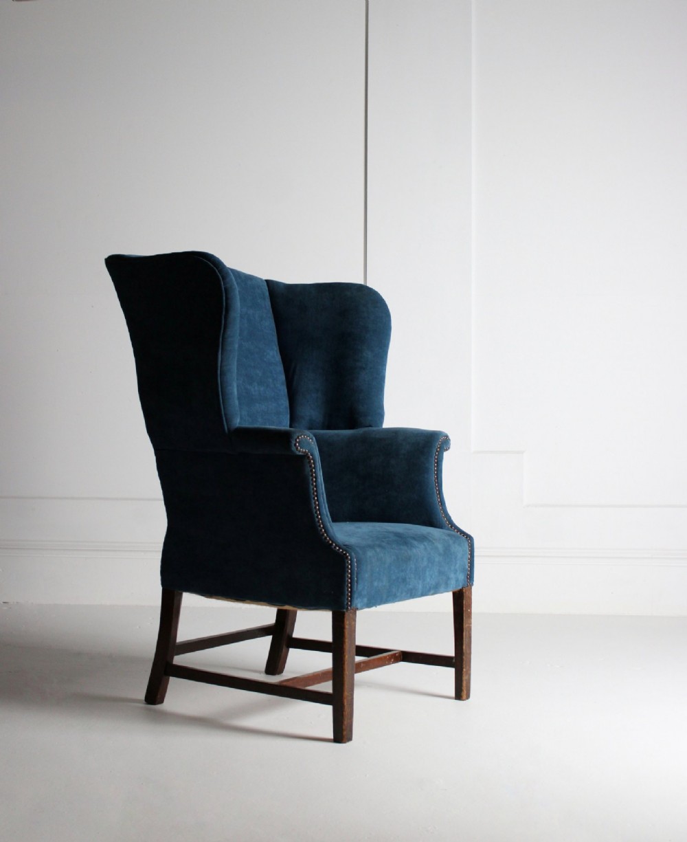 An early 20th-century wingback armchair upholstered in deep blue velvet with brass stud detail and dark wooden legs.