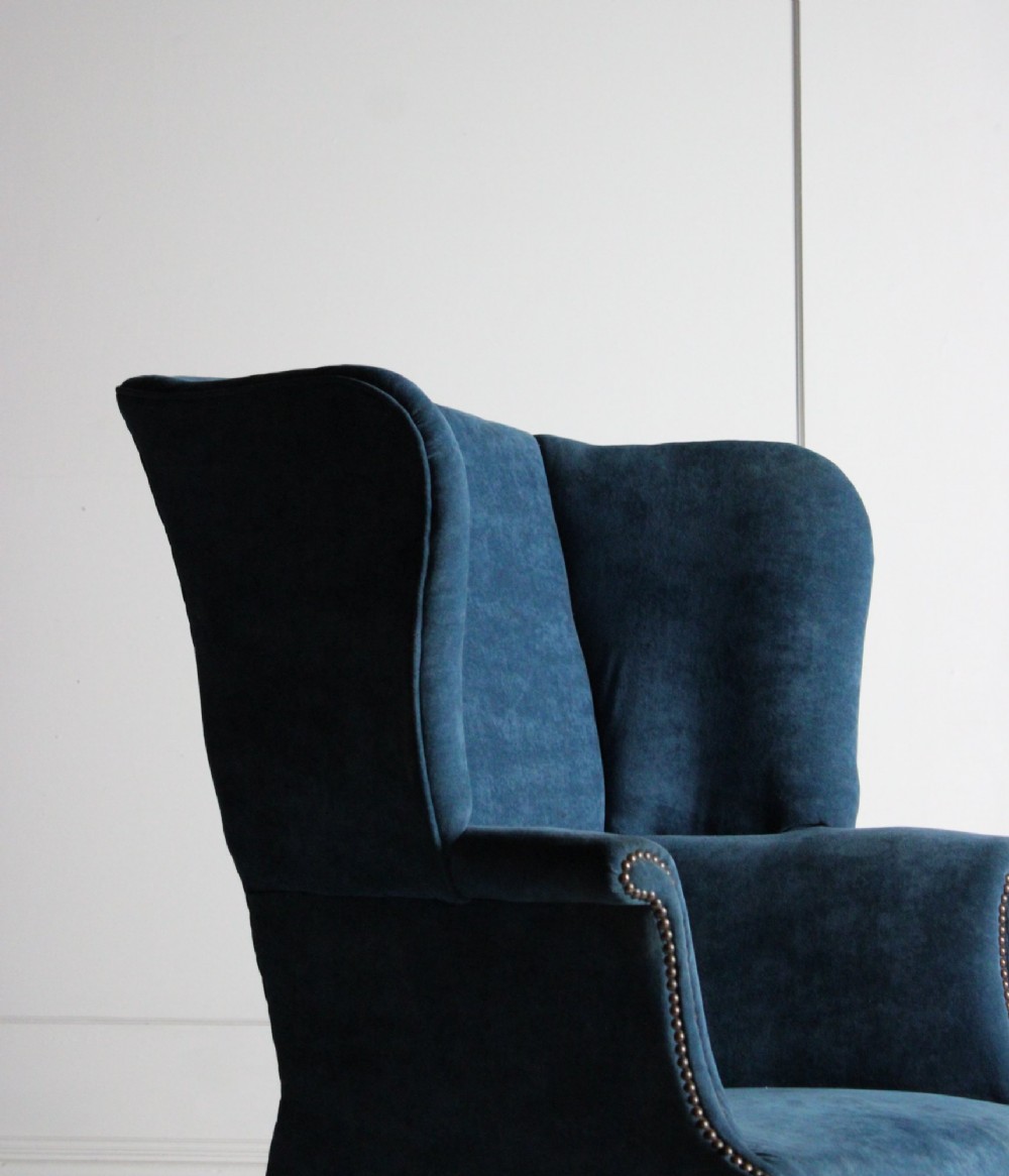 An early 20th-century wingback armchair upholstered in deep blue velvet with brass stud detail and dark wooden legs. View II