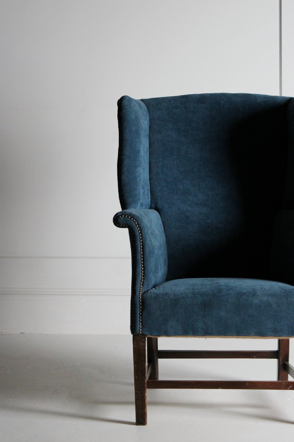 An early 20th-century wingback armchair upholstered in deep blue velvet with brass stud detail and dark wooden legs. View III