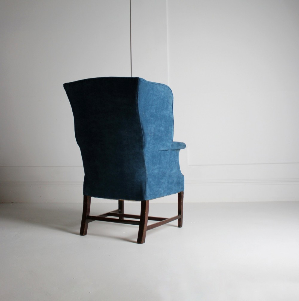 An early 20th-century wingback armchair upholstered in deep blue velvet with brass stud detail and dark wooden legs. View IV