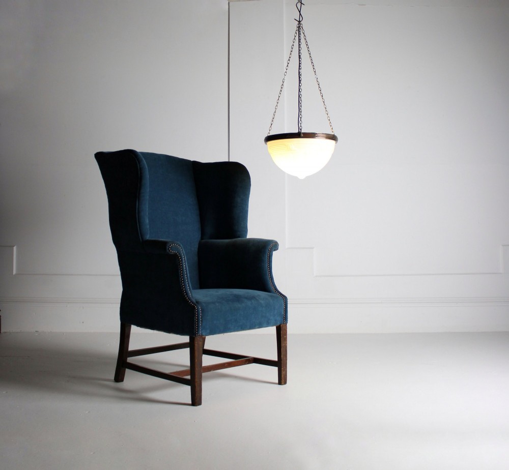 An early 20th-century wingback armchair upholstered in deep blue velvet with brass stud detail and dark wooden legs. View V
