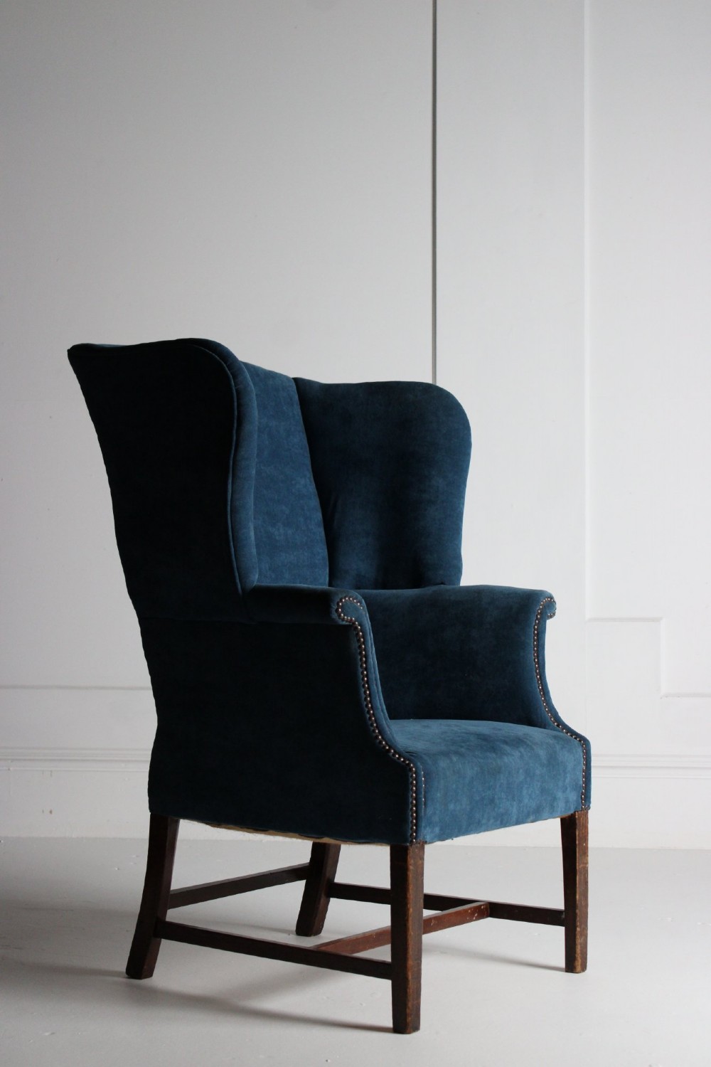 An early 20th-century wingback armchair upholstered in deep blue velvet with brass stud detail and dark wooden legs. View VI