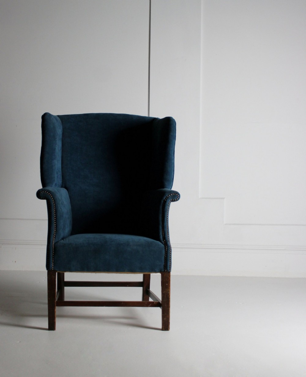 An early 20th-century wingback armchair upholstered in deep blue velvet with brass stud detail and dark wooden legs. View VII