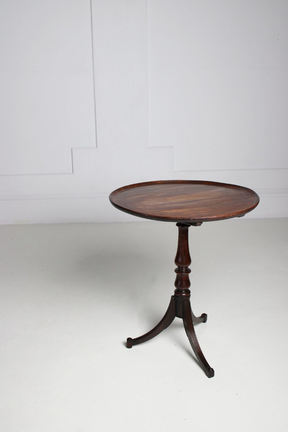 An antique Regency mahogany wine table featuring a rounded dish top on a turned pedestal stem and tripod splayed legs.