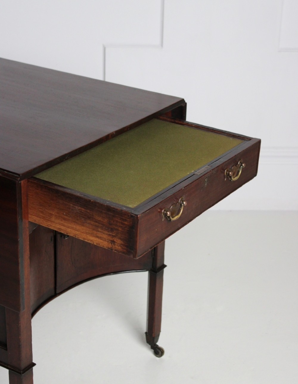 A George III mahogany side table featuring drop leaves, a single top drawer with brass handles, a concave lower cupboard, and square tapered legs on castors. View III