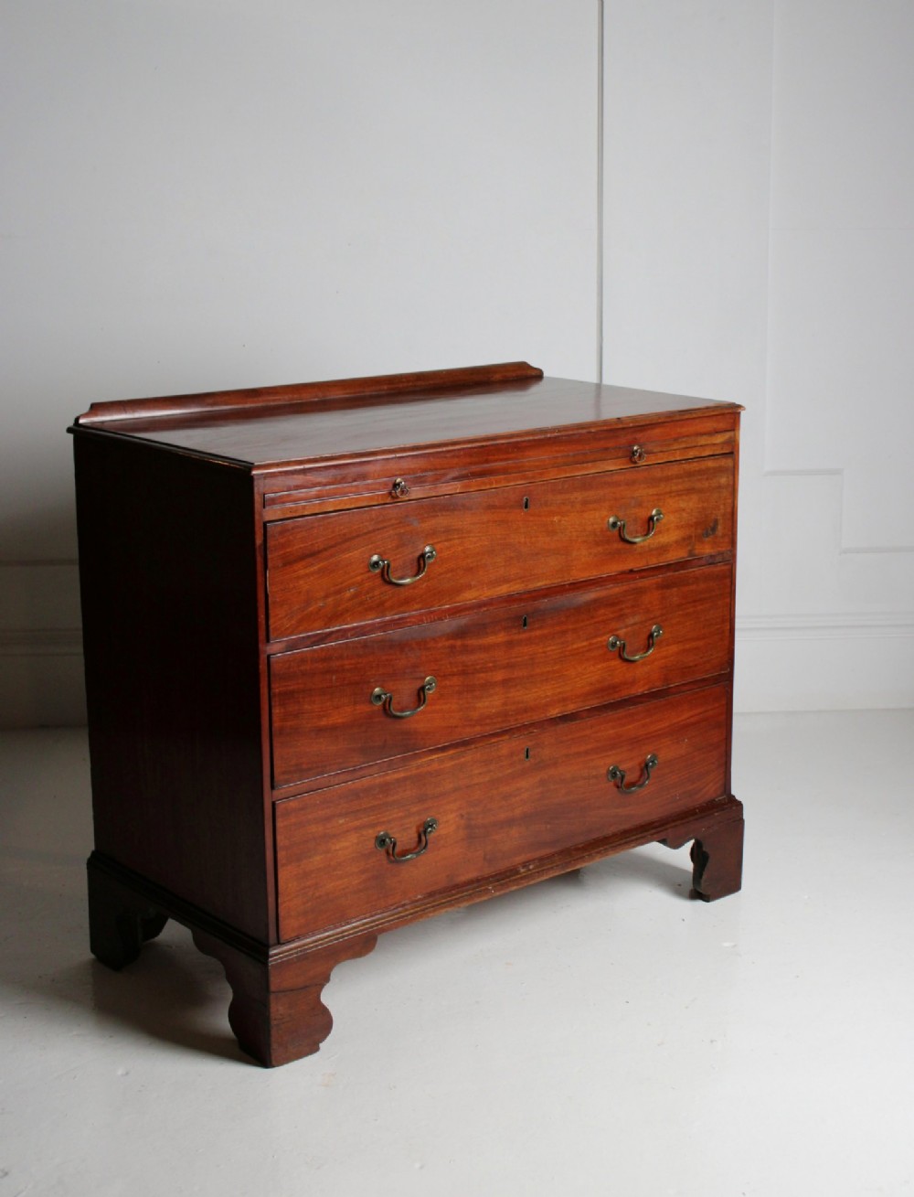 A George III mahogany chest of drawers featuring three graduated long drawers with brass swan-neck handles and bracket feet.